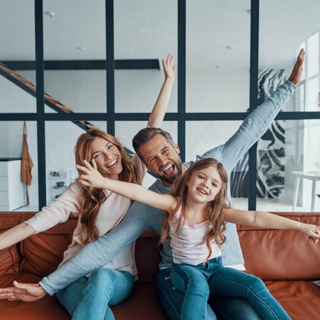 Happy family sitting on a couch with arms raised