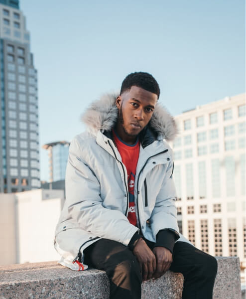 Portrait of Wade Warren, the President of Sales, sitting outdoors in a city wearing a white jacket with a fur hood.